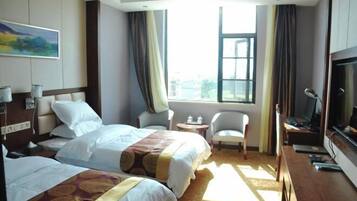 A hotel room with two beds, a desk with a computer, a TV, and a window with curtains.