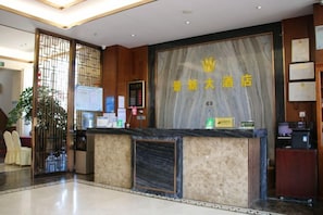 Un espace d’accueil d’hôtel avec un comptoir en marbre, un bureau d’accueil et une grande enseigne avec des caractères chinois.