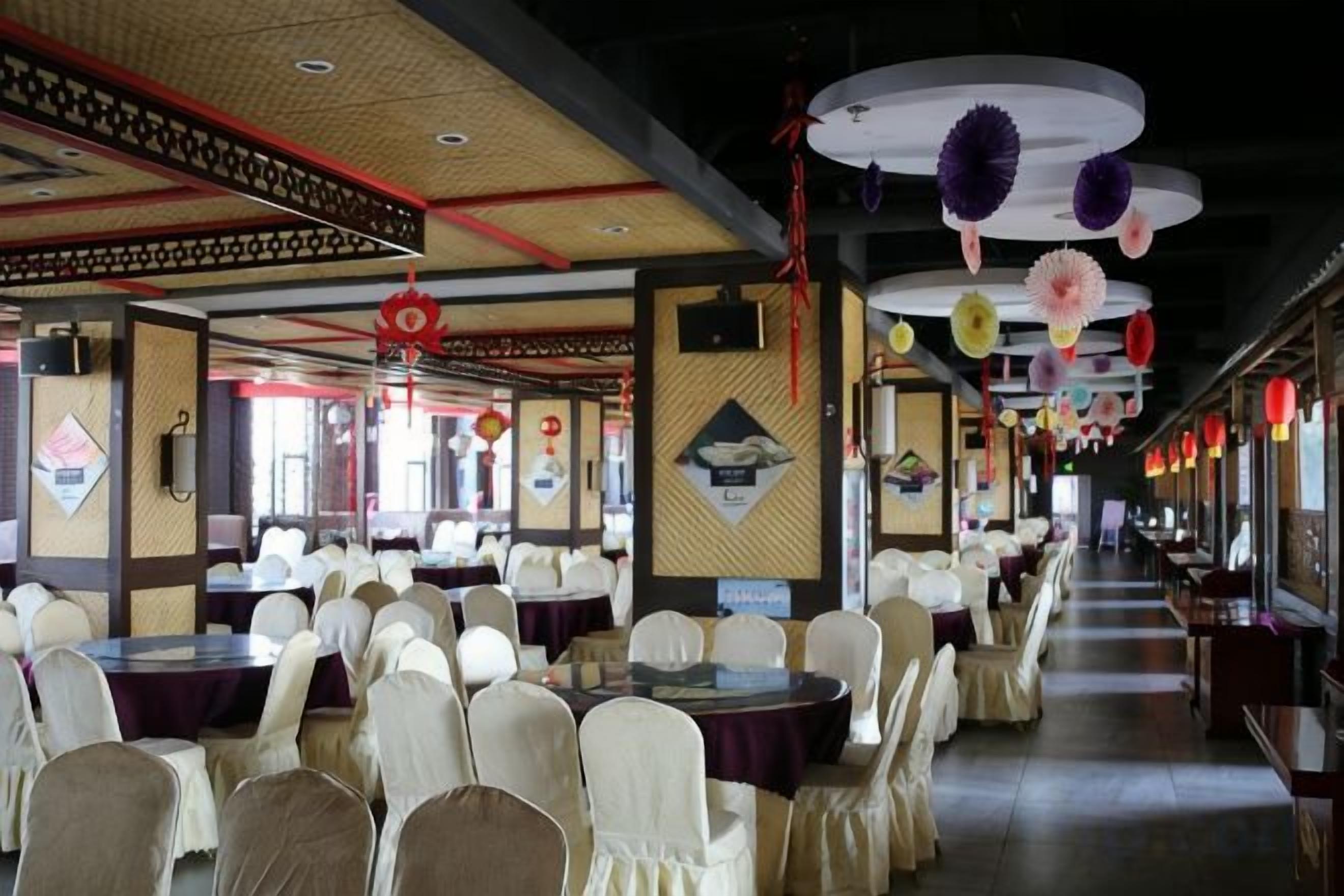 Une salle de banquet avec des tables et des chaises rondes, des lanternes rouges et des décorations murales traditionnelles.