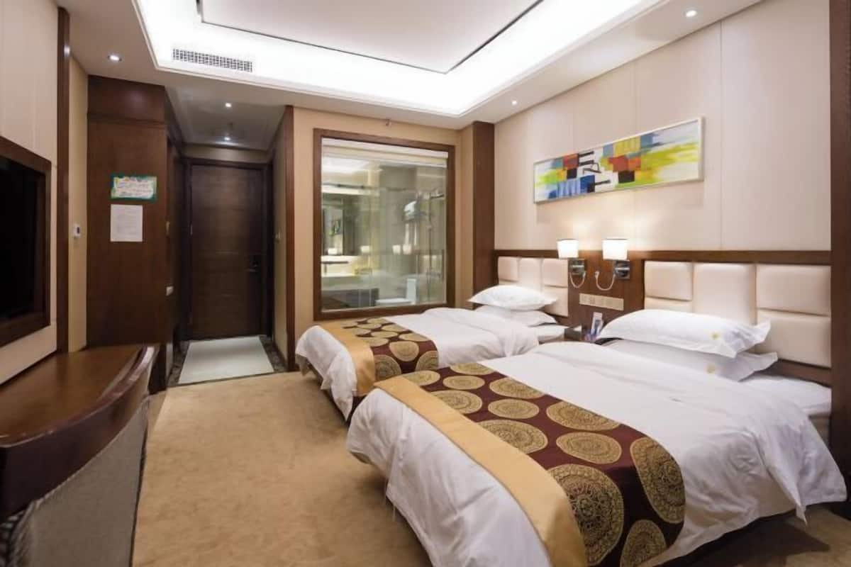 A hotel room with two beds, a TV, a desk, and a large window.