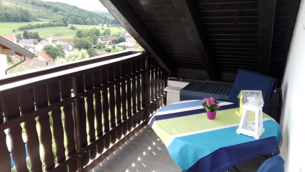 A balcony with a view of a village, a table with a tablecloth, a potted plant, and a lantern. - Vacation apartment with great views and hiking trails right outside the door (Burladingen)