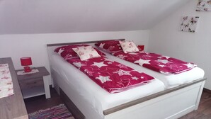 A double bed with a white frame and a red and white patterned bedspread. There is a small bedside table with a red lamp and a red cup. A colorful striped rug is on the floor. - Vacation apartment with great views and hiking trails right outside the door (Burladingen)