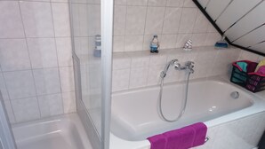 A bathroom with a shower, a bathtub, and a shelf with toiletries. - Vacation apartment with great views and hiking trails right outside the door (Burladingen)