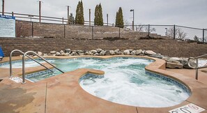 A spa area with two hot tubs and a pool, surrounded by a brick wall and a fence.