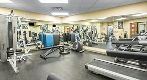 A gym with various exercise equipment, including treadmills, weight machines, and a mirrored wall.