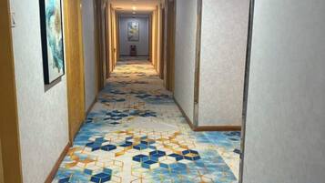 A hallway with patterned carpet, doors on both sides, and a framed picture on the left wall.