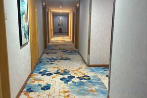 Un couloir avec un tapis à motifs, des portes de part et d’autre, et un tableau encadré sur le mur de gauche.