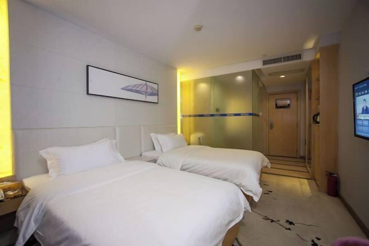 Hotellihuone, jossa on kaksi sänkyä, televisio ja seinällä oleva kehystetty taulu.