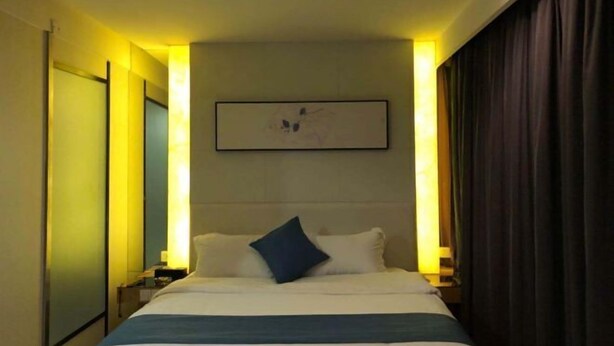 Ein Hotelzimmer mit Bett, Nachttischen, einem Wandbild und einem Vorhang auf der rechten Seite.