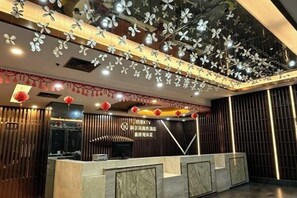 Un espace d’accueil d’hôtel au design moderne, comprenant un comptoir de réception, des éléments décoratifs au plafond et une enseigne indiquant le nom de l’hôtel.