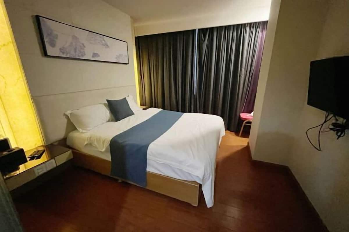 Hotellihuone, jossa on sänky, yöpöytä, televisio ja ikkuna, jossa on verhot.