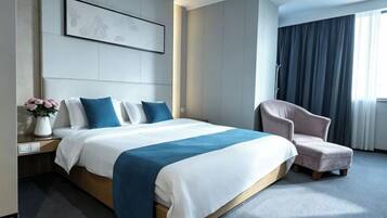 A modern hotel room with a large bed, a chair, a nightstand, and a window with curtains.