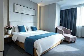Ein modernes Hotelzimmer mit einem großen Bett, einem Sessel, einem Nachttisch und einem Fenster mit Vorhängen.