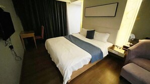 A hotel room with a large bed, a bedside table, a chair, a TV, and a curtain. - Ke'erma Business Hotel (Zhongshan)