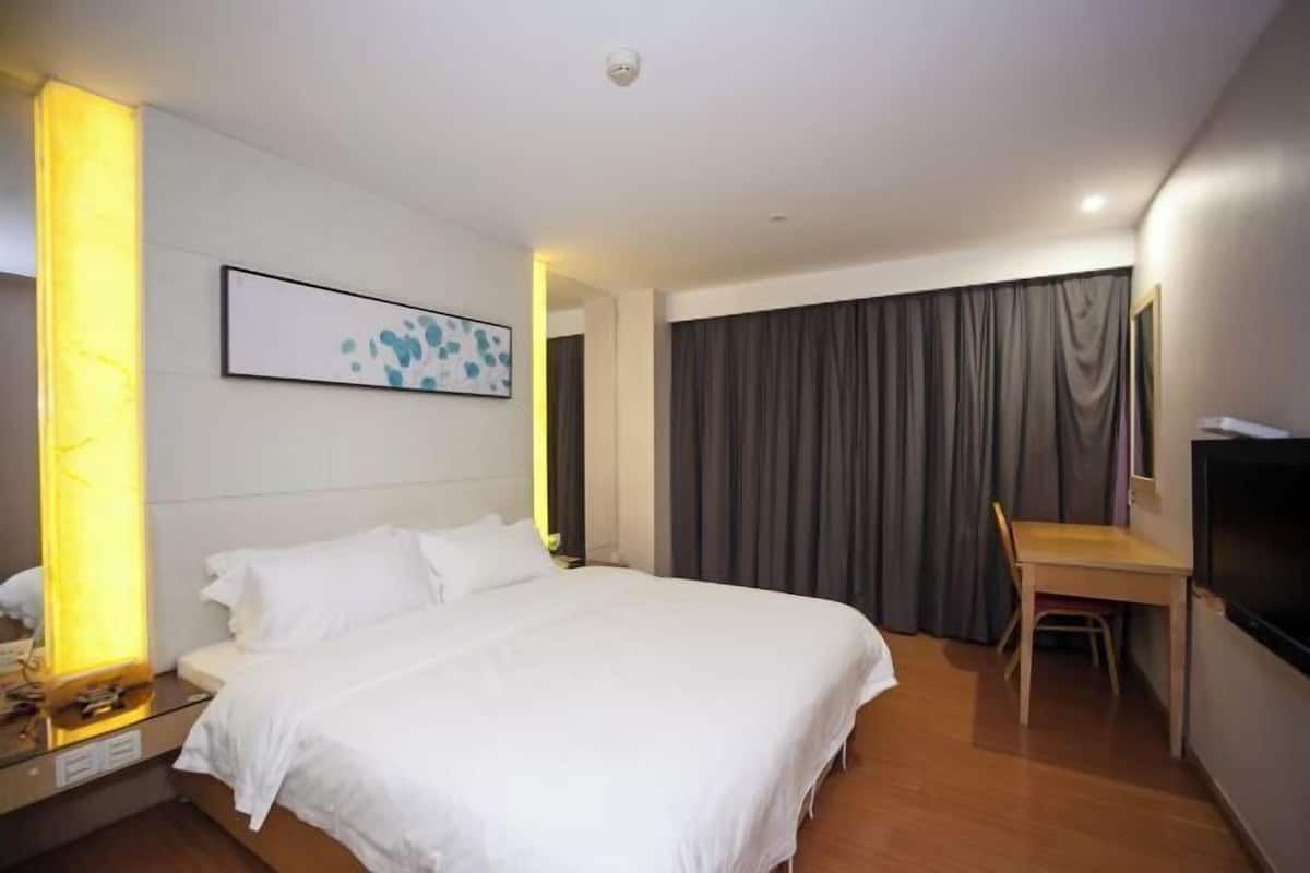 Hotellihuone, jossa on suuri sänky, työpöytä, tuoli, taulutelevisio ja taulu seinällä.
