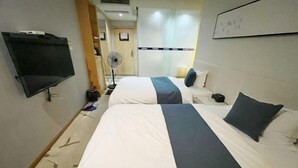 Camera d'albergo con due letti, una TV a schermo piatto, una ventola e una lavagna a parete.
