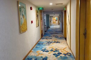 A hotel corridor with patterned flooring, framed artwork on the walls, and doors on the right.