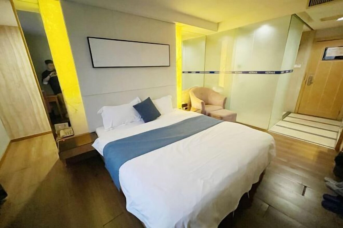 A hotel room with a bed, a chair, a wardrobe, and a mirror.