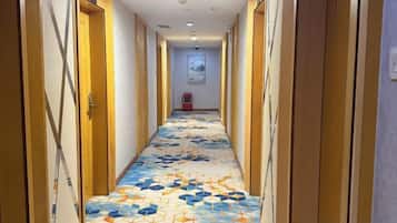 Un pasillo de hotel con alfombra estampada, puertas de madera y un cartel en la pared.
