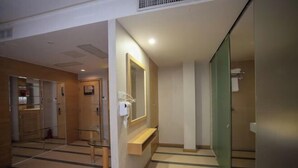 Ein Hotelgang mit einem Spiegel, einer Bank und einer Glastür zu einem Badezimmer.