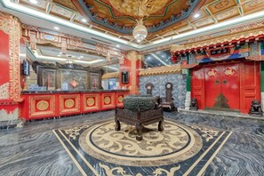 A room with a traditional design, featuring a central bed, a red wall with decorative elements, and a patterned floor.