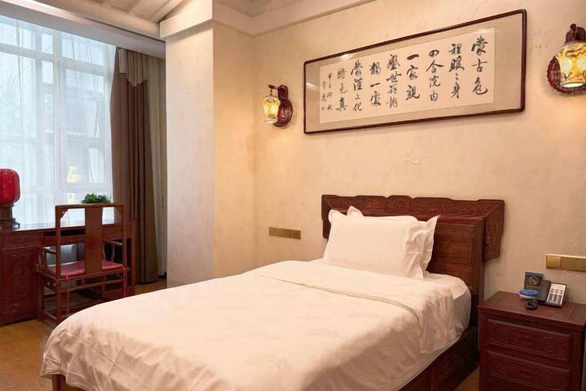 Une chambre d’hôtel avec un grand lit, une table de chevet en bois, un bureau avec une chaise et une fenêtre avec des rideaux.