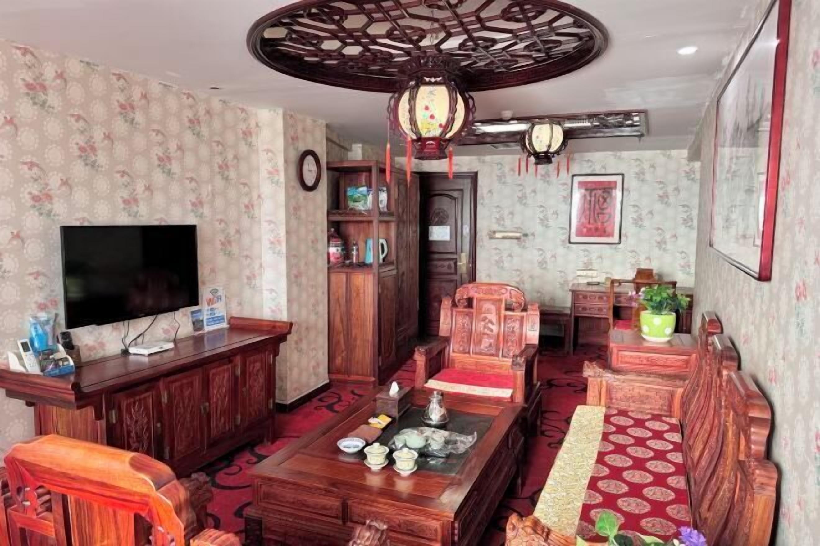 A traditional living room with a television, wooden furniture, and a decorative ceiling fan.