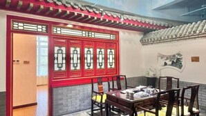 Ein traditionell eingerichteter Raum im chinesischen Stil mit roter Tür, einem Esstisch mit Stühlen und einer Wandmalerei.