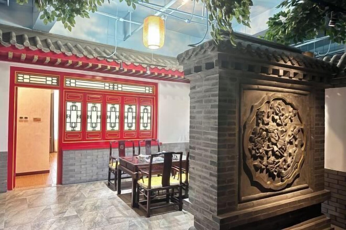 Quarto em estilo tradicional chinês, com portas vermelhas, parede de pedra com esculturas e uma mesa de jantar com cadeiras.
