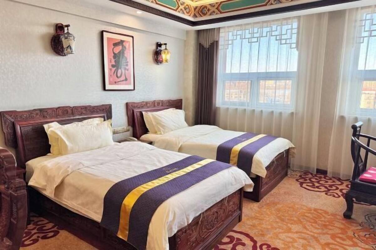 Une chambre d’hôtel avec deux lits en bois, une moquette à motifs, une fenêtre avec des rideaux et des lampes fixées au mur.
