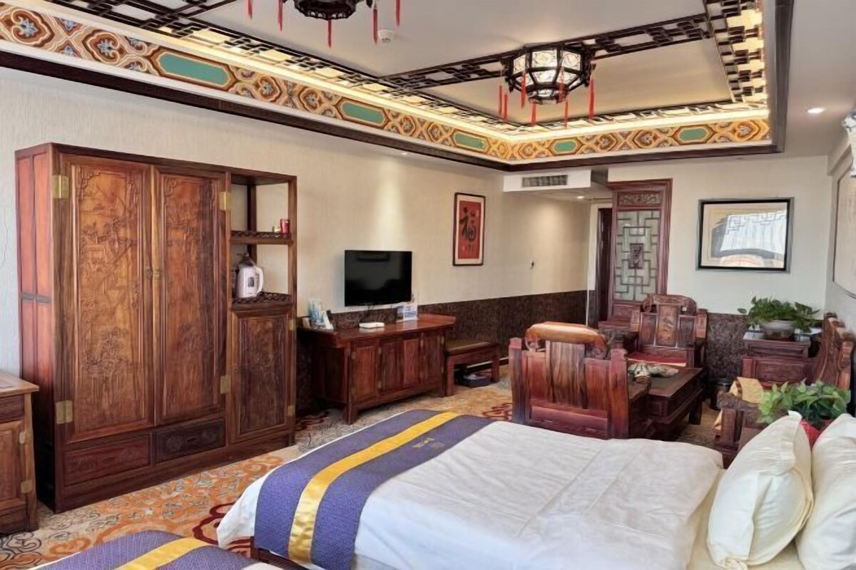 Quarto tradicional com cama grande, móveis de madeira, televisão e padrões decorativos nas paredes.