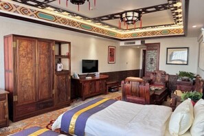 Quarto tradicional com cama grande, móveis de madeira, televisão e padrões decorativos nas paredes.
