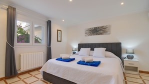 A hotel room with a large bed, a window with curtains, a radiator, a wall art piece, and a nightstand with a lamp. - Arundel - Javea, Costa Blanca (Javea)