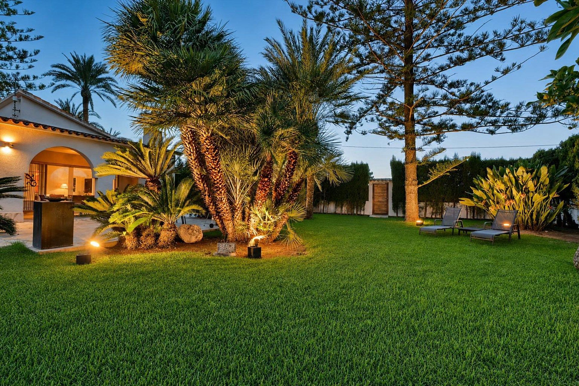 A well-maintained lawn with a patio area, outdoor seating, and a variety of tropical plants.