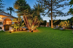 Ein gepflegter Rasen mit einer Terrassenfläche, Gartenmöbeln und verschiedenen tropischen Pflanzen.