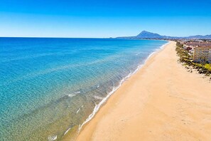 A coastal beach with clear waters, a sandy shore, and a mountain in the distance.