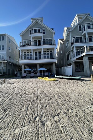 A beachfront property with a large building, outdoor seating with umbrellas, and a kayak. - Luxurious, Direct Waterfront Home with Private Beach (Milford)