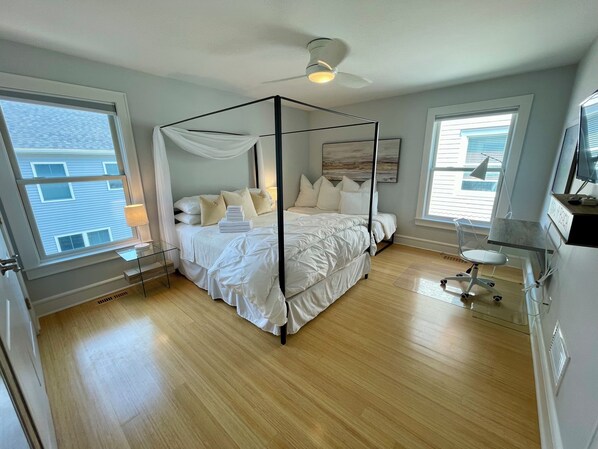 A four-poster canopy bed with white bedding, a bedside table, and a lamp.
