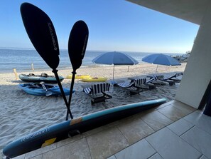 A beachside view with kayaks, lounge chairs, and umbrellas. - Luxurious, Direct Waterfront Home with Private Beach (Milford)