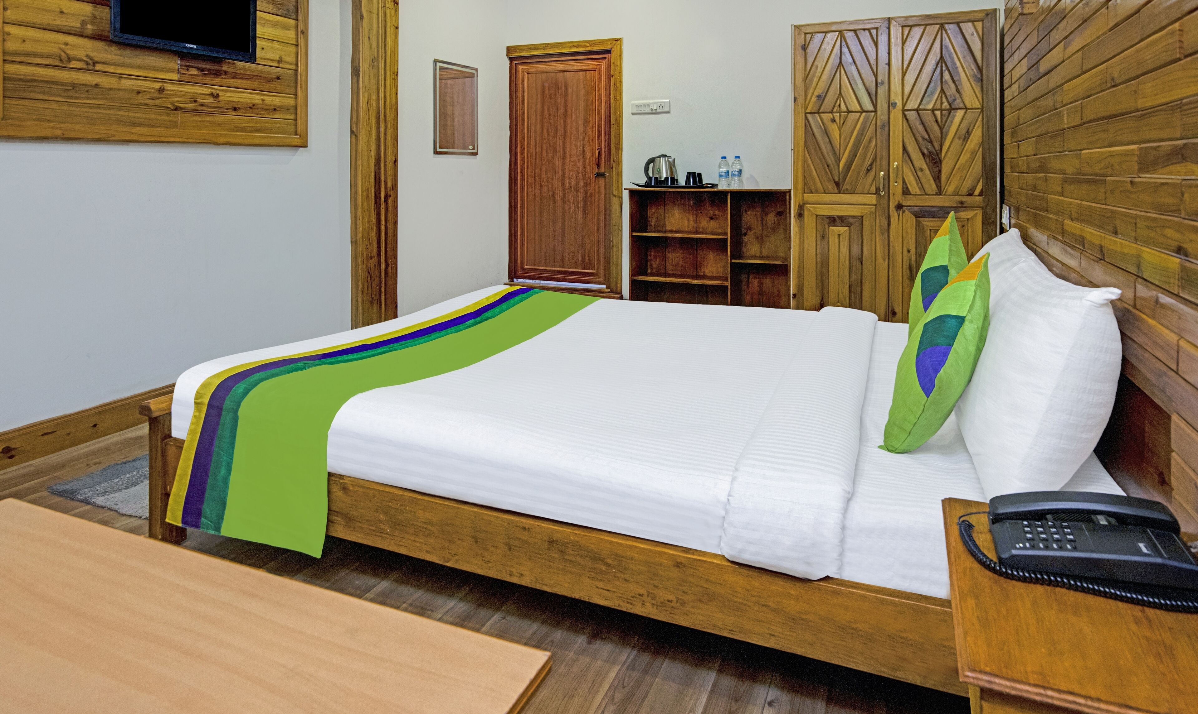 Een net opgemaakt bed met een kleurrijke deken, een bedtelefoon en een houten nachtkastje.