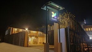 Entrada de hotel con un cartel moderno, acceso mediante portón y fachada de edificio bien iluminada.