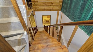 Una escalera de madera con barandilla que conduce a una habitación con techo de madera y una cortina verde.