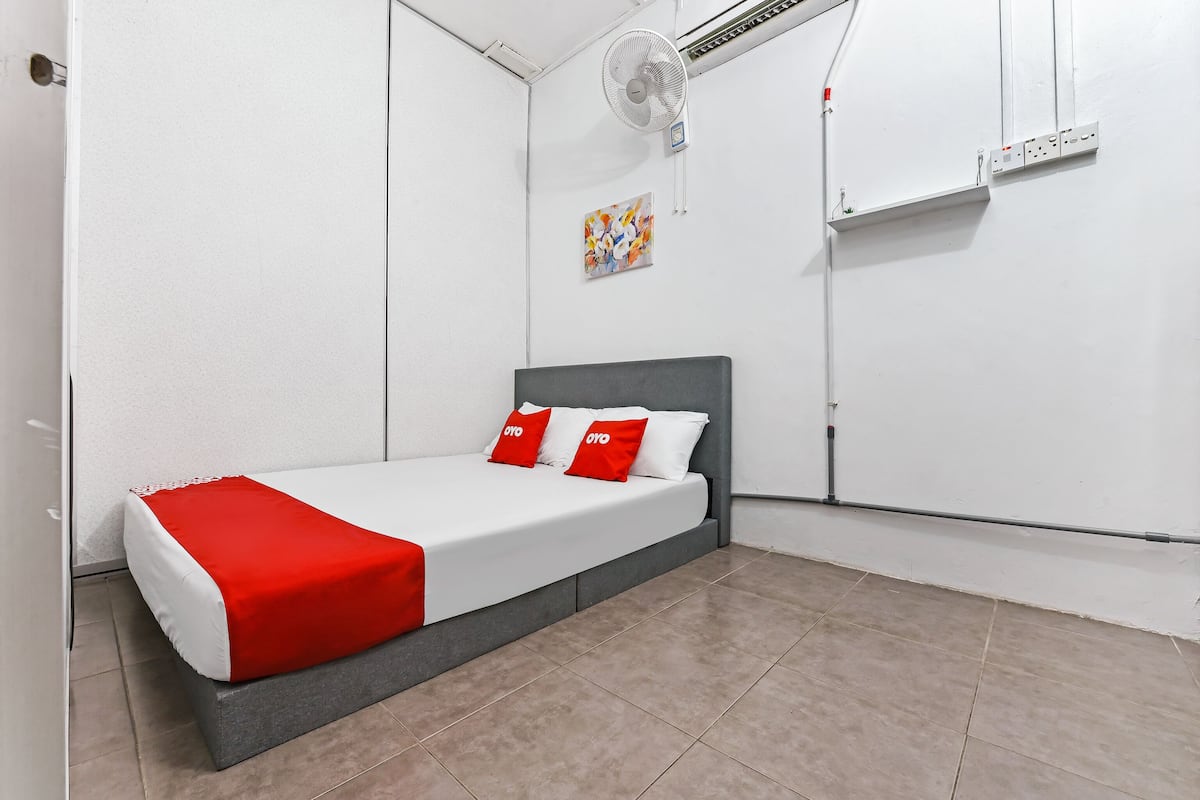 A single bed with a grey headboard, white bedding, and red pillows. There is a white wall with a small abstract painting and a whiteboard.