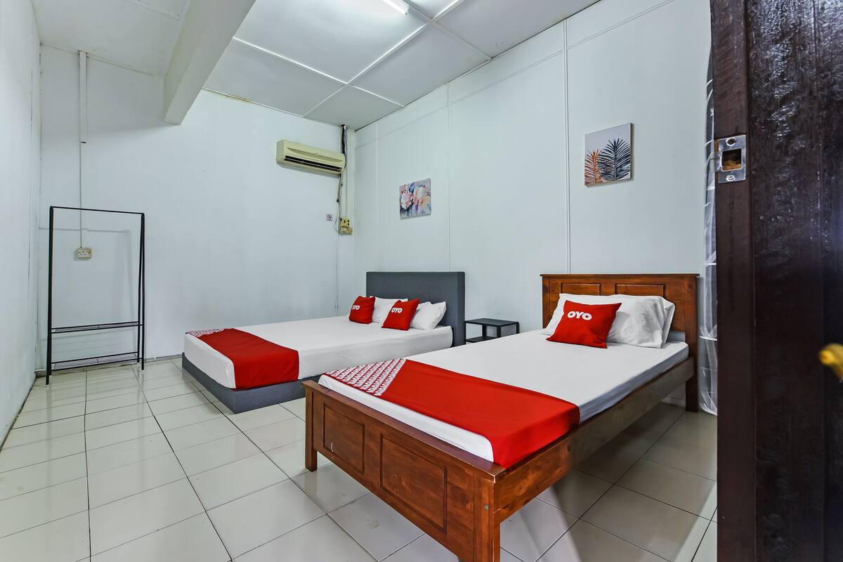 A hotel room with two single beds, each with red and white bedding, a wooden headboard, and a small bedside table.