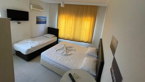 Une chambre d’hôtel avec deux lits simples, une petite table ronde, un téléviseur fixé au mur et une fenêtre avec des rideaux.