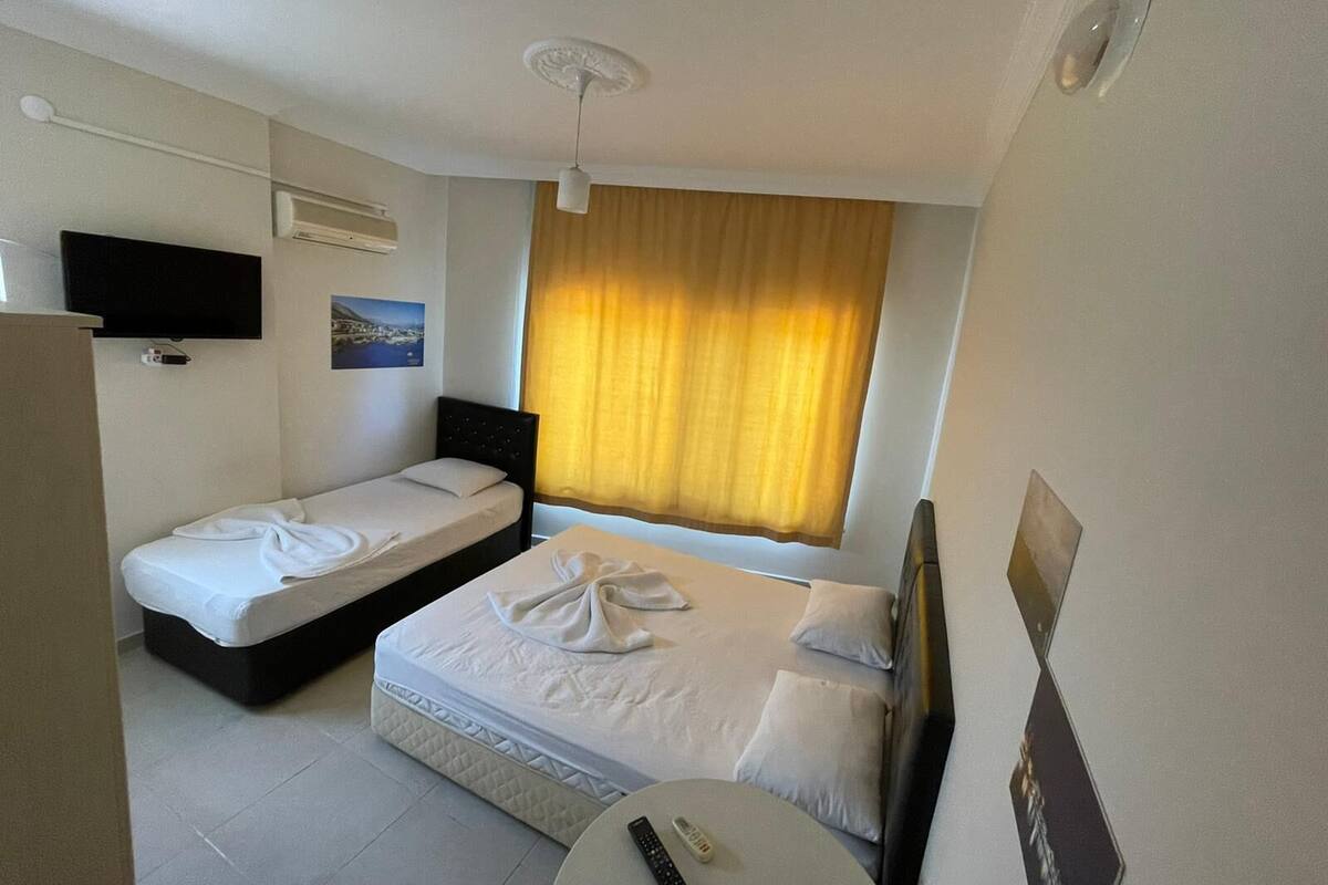 Een hotelkamer met twee eenpersoonsbedden, een klein rond tafeltje, een aan de muur bevestigde televisie en een raam met gordijnen.