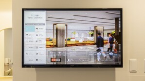 Une chambre d’hôtel équipée d’un grand téléviseur à écran plat affichant un plan de la chambre et une liste des équipements disponibles.