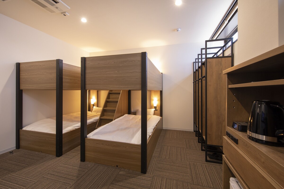 Habitación de hotel con literas, una escalera, una cafetera y un estante con una tetera.
