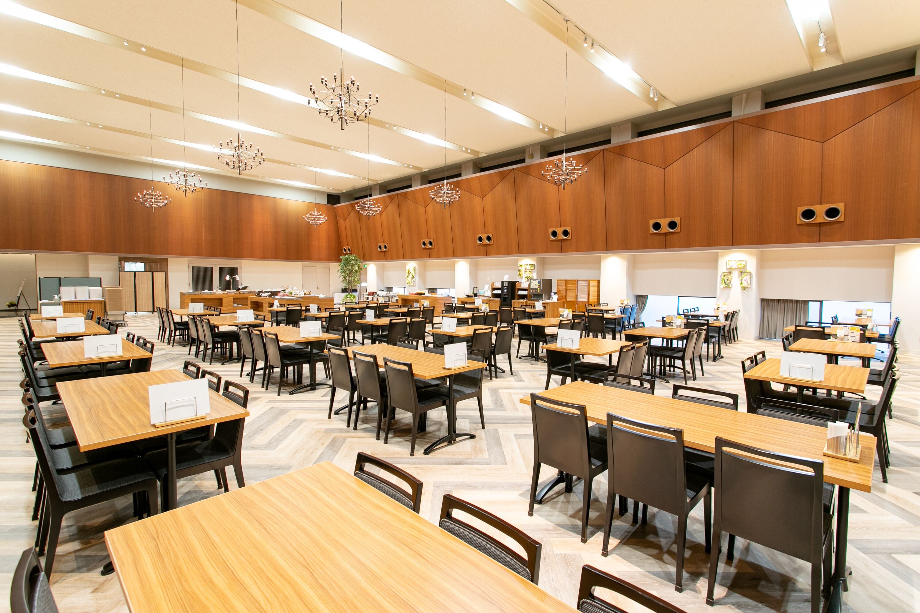 Un'ampia sala conferenze ben illuminata, con numerosi tavoli e sedie, pannelli di legno alle pareti e moderni lampadari.