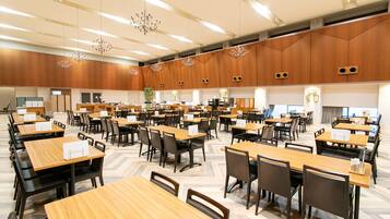 Un'ampia sala conferenze ben illuminata, con numerosi tavoli e sedie, pannelli di legno alle pareti e moderni lampadari.
